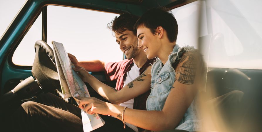 Smiling couple looking at map sitting in truck on road trip