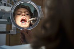 Dentist checking boy using mouth mirror in office