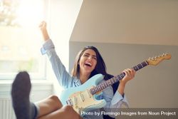 Woman having fun and laughing while playing guitar at her desk 5RvaA5