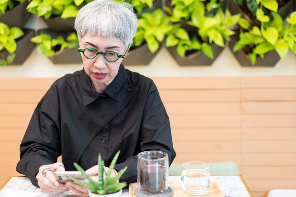 Trendy grey haired woman sitting in cafe looking at phone
