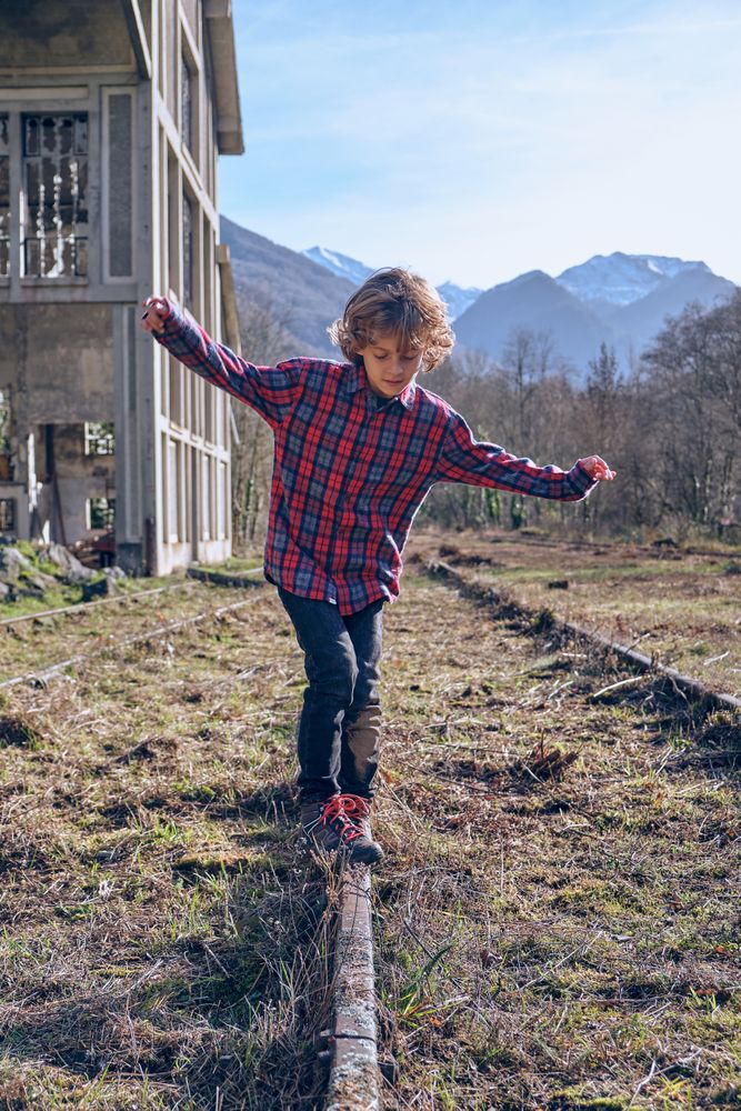 Boy spreading arms while balancing on rail in suburb area