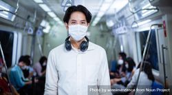 Portrait of man in facemask and headphones standing in metro car 0KqrZ4