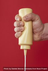 Squeezing a mayonnaise bottle isolated on a red background 0gw7l0