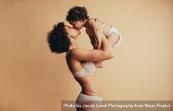 Woman with curly hair holding up her baby and kissing her bxY9M0