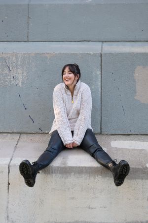 Woman smiling and sitting on gray concrete floor