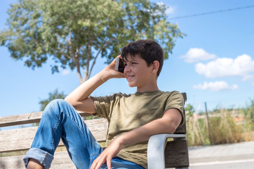 Boy sitting on bench speaking on phone
