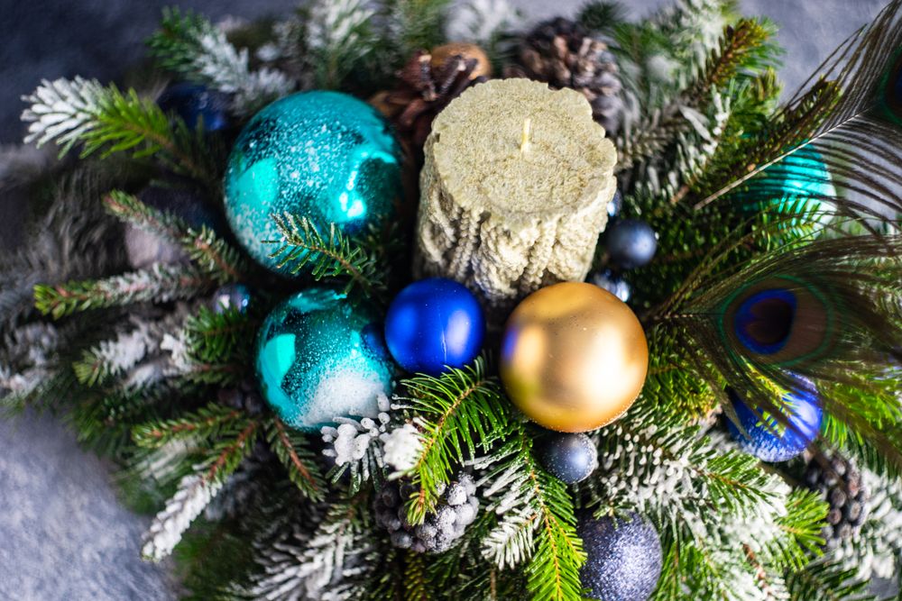 Blue and gold Christmas baubles in pine centerpiece with candle and peacock feathers