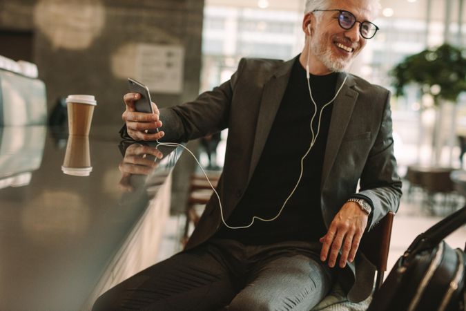 Happy mature businessman sitting at cafe listening music for cellphone