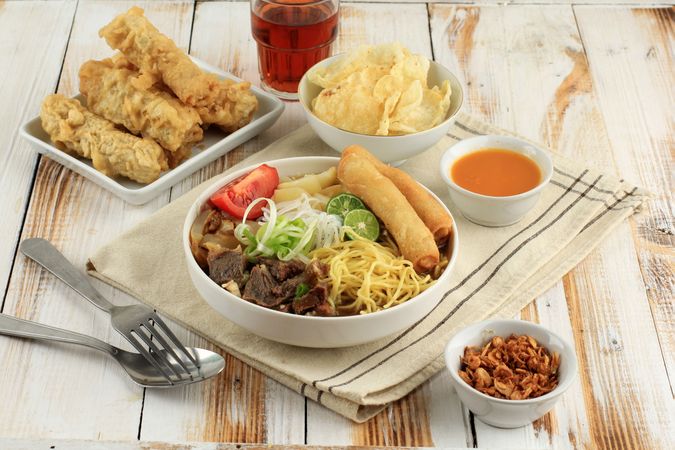 Indonesian beef noodle soup with noodles, beef, spring roll, cabbage and tomato