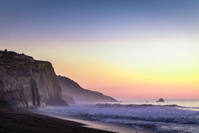Cliffs on beach at sunset as waves come in