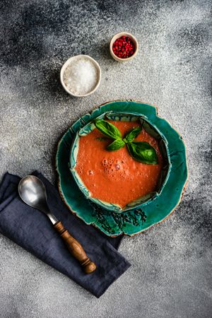Top view of traditional Spanish tomato soup Gazpacho in green bowl served with basil, salt & pepper with copy space