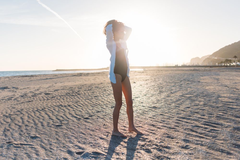 Woman with her arms up on beach at sunset in oversized shirt