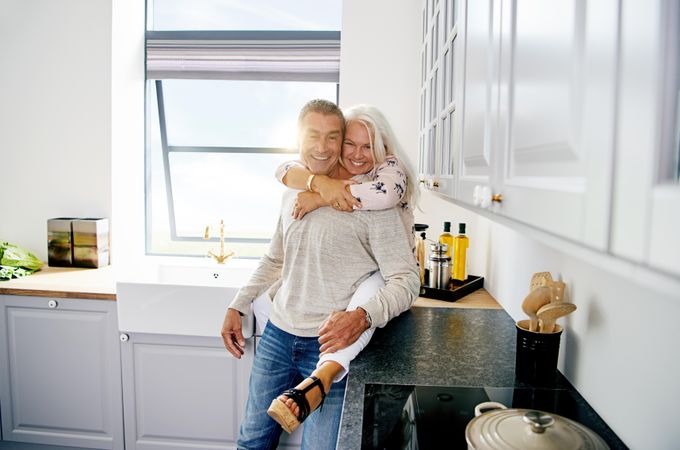 Happy mature couple in kitchen with woman sitting on counter
