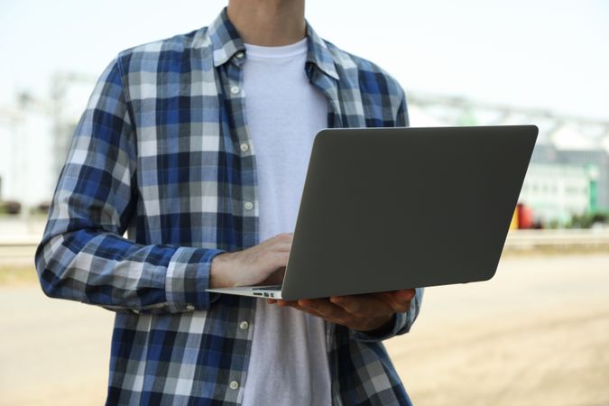 Young man with laptop against grain silos. Agriculture business