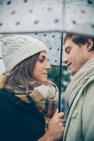 Cute couple facing each other under the umbrella on an autumn rainy day