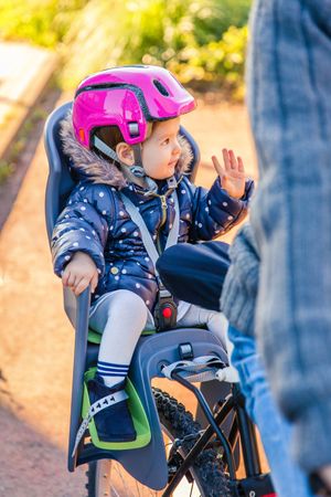 Portrait of little girl with pink helmet on waving in bike seat in back of ride