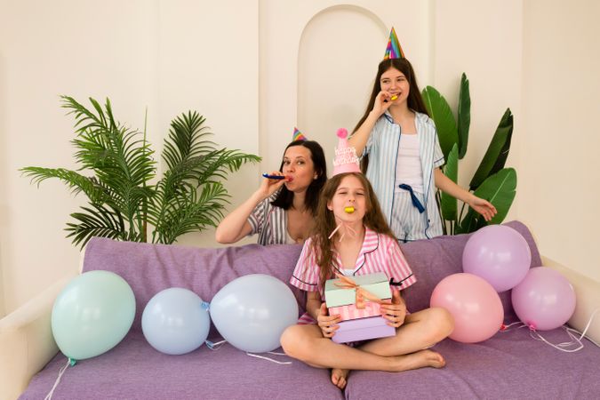 Mother and daughters playing with party whistles at birthday celebration.