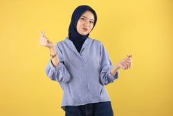 Smiling Asian Woman in Blue Striped  Shirt and Navy Hijab  Showing Korean Heart with Two Fingers Crossed