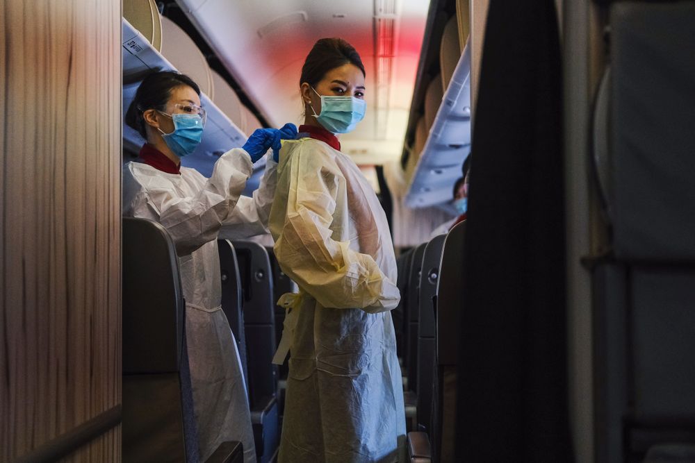 Two flight attendants with facemask and protective apron standing in airplane