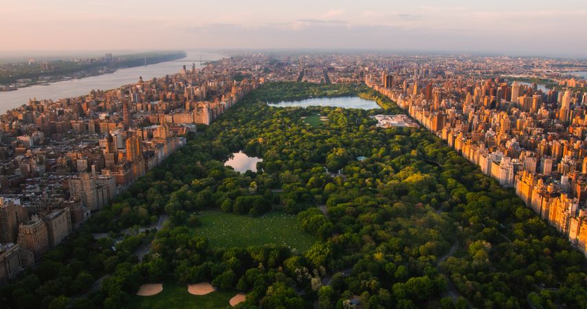 New York Cityscape at Sunset. Aerial Shot from a Helicopter. Modern Skyscraper Buildings Around Central Park in Manhattan Island. Focus on Nature, Trees and Lakes in the Park in the City