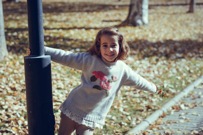Happy child hanging from lamp post in field of colorful fall leaves