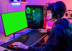 White young man plays computer in his room with colored lights and looks at the screen concentrated