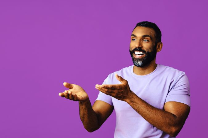 Male speaking in purple t-shirt with hands gesturing to copy space in bright purple studio