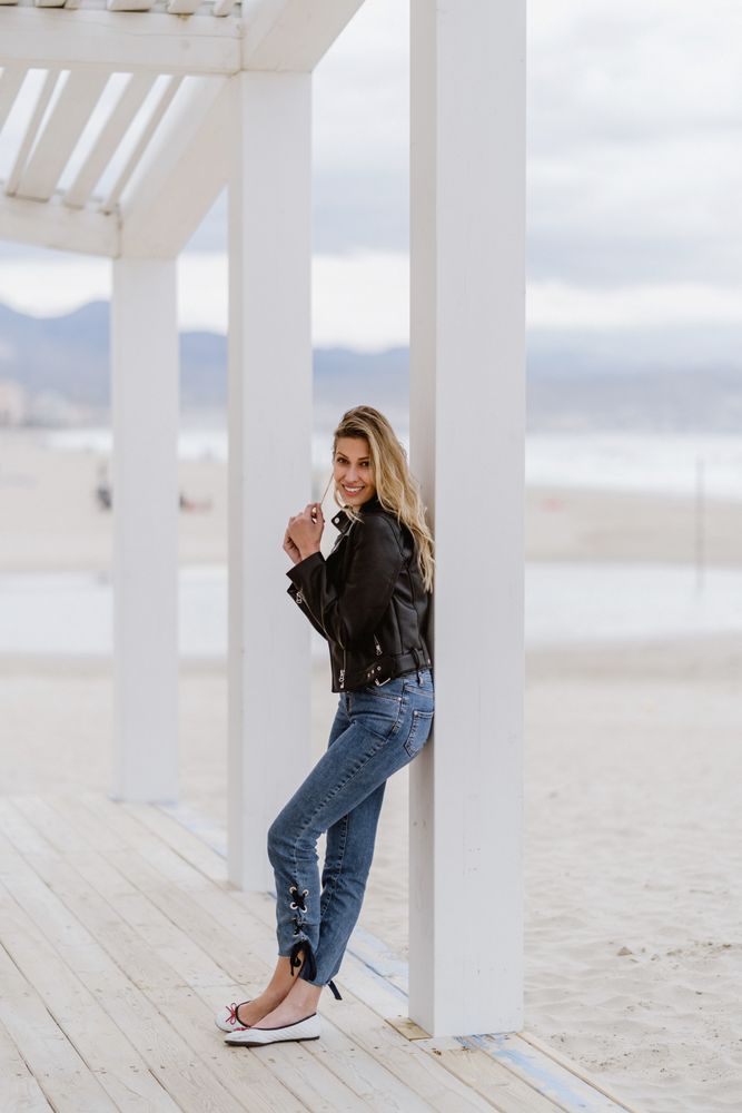 Smiling trendy woman leaning on white pillar on seashore
