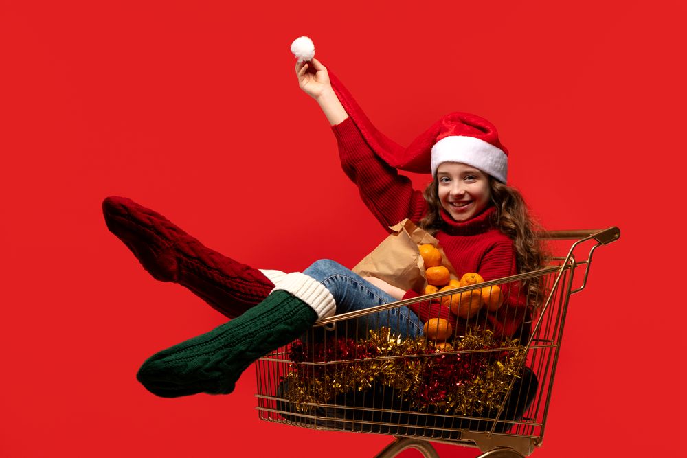 Teen girl in Santa hat in shopping cart with oranges.