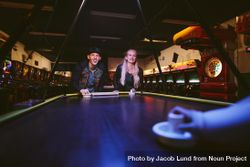 Man and woman playing a game of air hockey in the game room at amusement park 0WanM4
