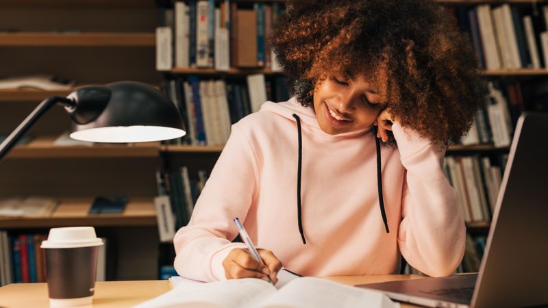 Student sitting at desk writing notes in front of laptop