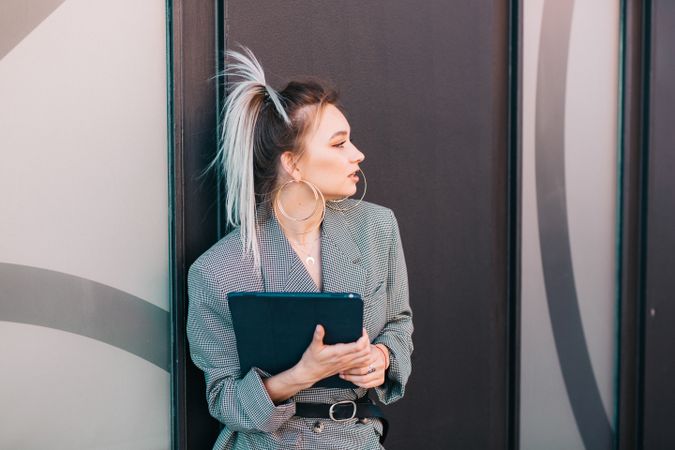 Stylish businesswoman with laptop leaning on wall