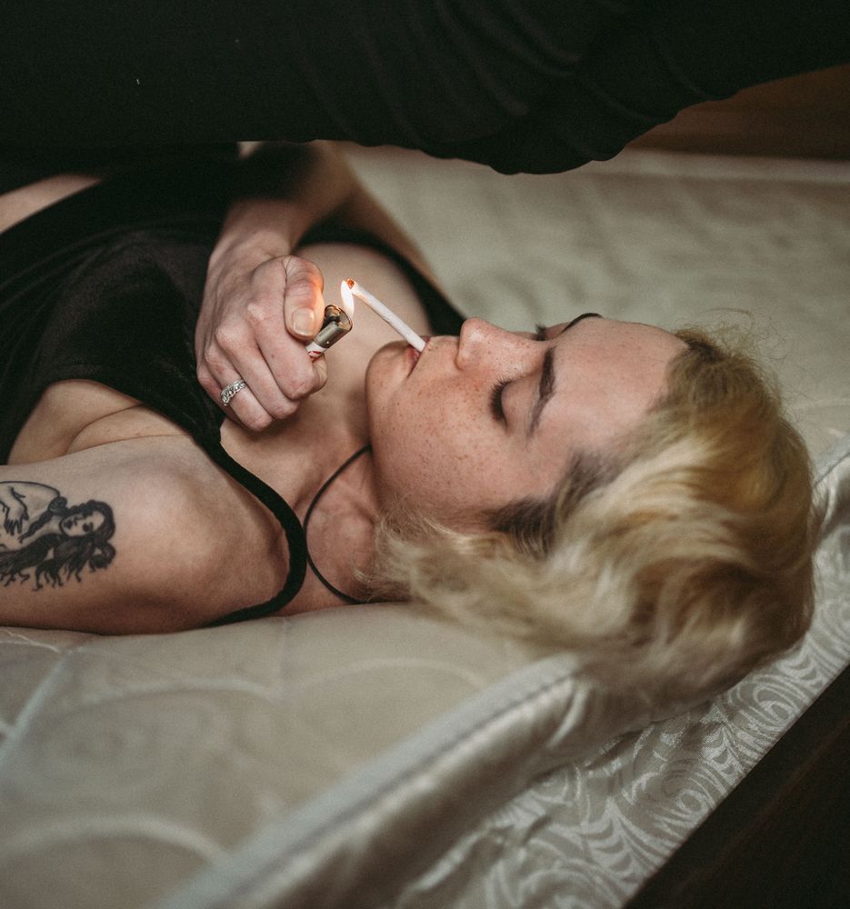 Confident pensive freckled woman smoking on bed
