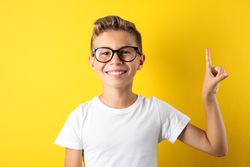 Happy boy in glasses against yellow background, space for text