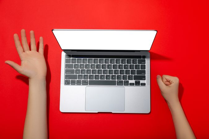 Top view of person’s hands next to laptop keyboard on red table