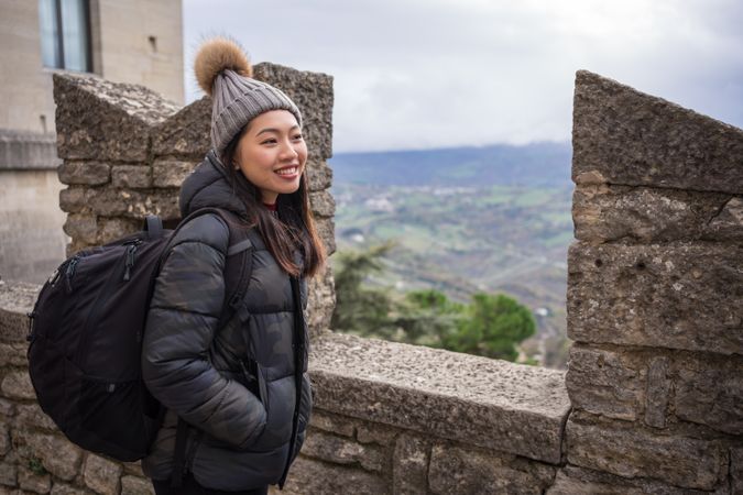 Relaxed Asian woman in warm hat with pompom sightseeing and looking at city down