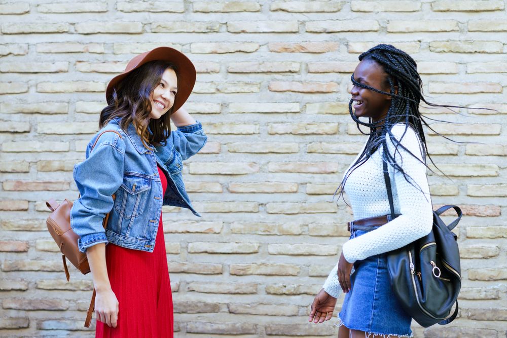 Two women facing each other and talking beside a brick wall