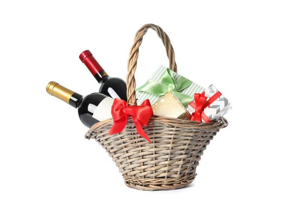 Wicker basket with bottles of wine and presents isolated on light background