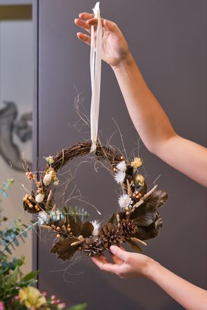 Crop florist demonstrating dried wreath