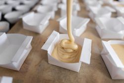 A baker woman is filling paper molds to prepare cupcakes. Close up