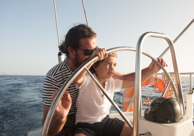 Man and boy holding steering wheel on yacht on water