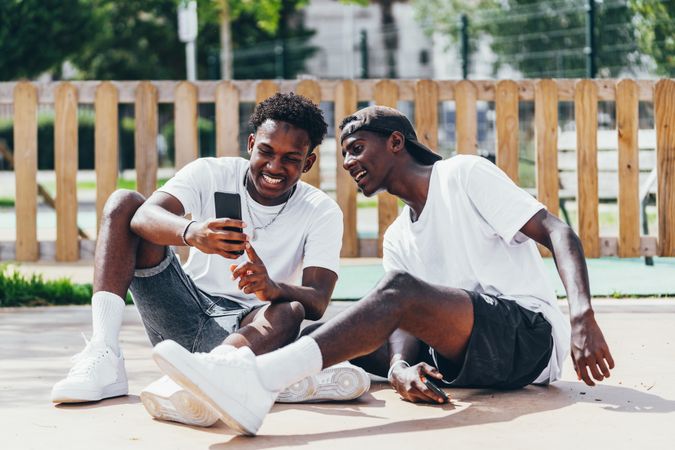 Excited sportive black men looking browsing smartphone while sitting on ground