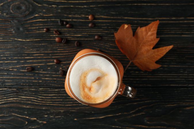 Glass jar of pumpkin latte, coffee seeds and leaf on wooden background