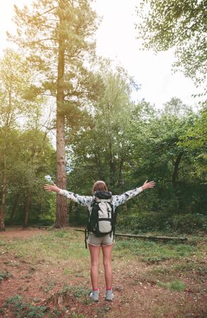 Hiker woman with backpack raising her arms facing the forest