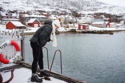 Woman on waterfront against small town at snowy foothill