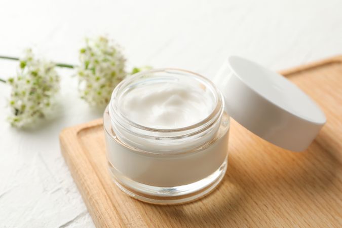 Jar with cream, allium flowers and board on blank background, closeup