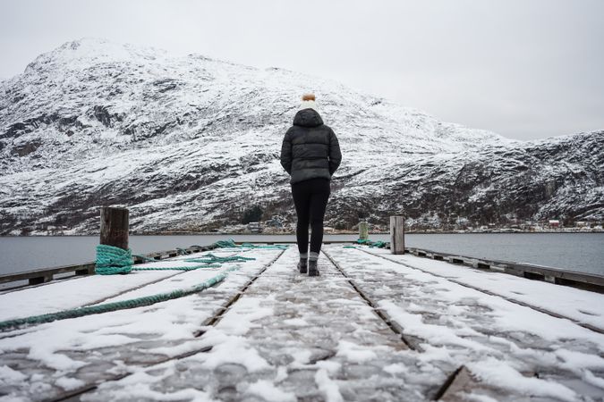Woman on waterfront against small town at snowy foothill
