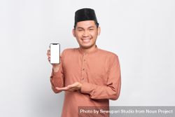 Happy Muslim man in kufi hat holding mobile phone and showing mock up screen 5XvxVb