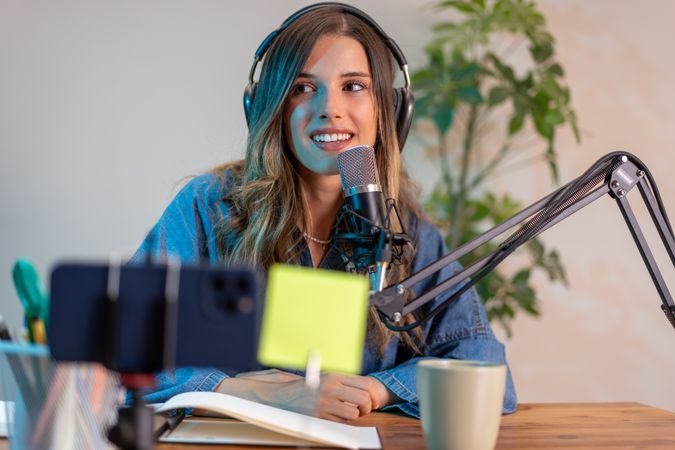 Young female content creator recording podcast using professional microphone and digital devices in modern home office studio