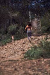 Unrecognizable sportswoman jogging on alley near dog in woods